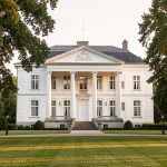 Comment vérifier si la Maison-Blanche est une copie du château de Rastignac ? Vue frontale réaliste du château de Rastignac en Dordogne, avec sa façade blanche néoclassique à colonnes et son parc arboré baigné d’une douce lumière de fin d’après-midi.