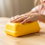 Quel budget faut-il prévoir pour acheter un squishy beurre anti-stress ? Squishy jaune en forme de motte de beurre posé sur une table claire, doucement pressé par la main d’une jeune fille, avec une lumière naturelle.